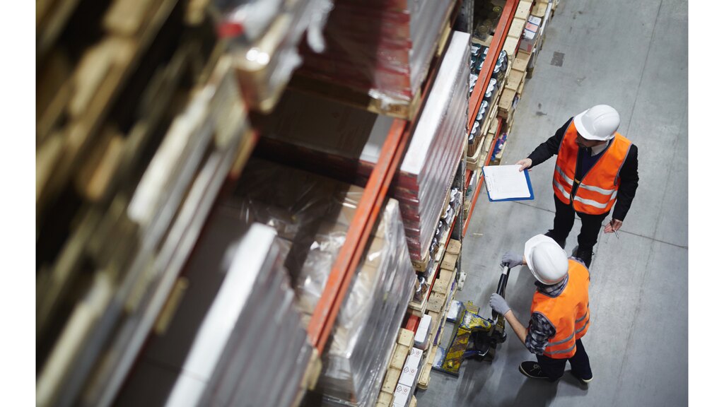 otimizacao fluxo logistico analise preditiva.jpg Vista aérea de trabalhadores em um centro de distribuição operando transpaleteira e conferindo inventário, exemplificando a eficiência operacional guiada por análise preditiva na logística.