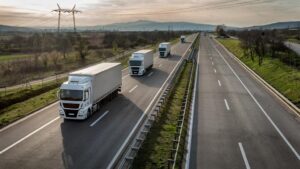 Caminhões realizando transporte rodoviário em rodovia moderna, representando logística sustentável, eficiência operacional e otimização do transporte de cargas.