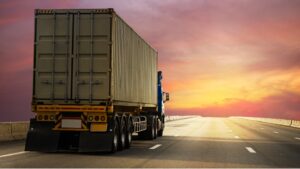 caminhão de carga transportando um contêiner em rodovia, representando a logística de transporte integrada aos sistemas de controle de estoque para garantir rastreabilidade, eficiência operacional e segurança na distribuição de mercadorias.