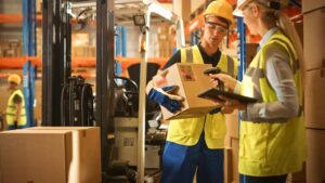 Profissionais realizam a conferência e preparação de pedidos em um armazém logístico, utilizando coletor de dados para garantir precisão, rastreabilidade e eficiência no processo de picking e packing.